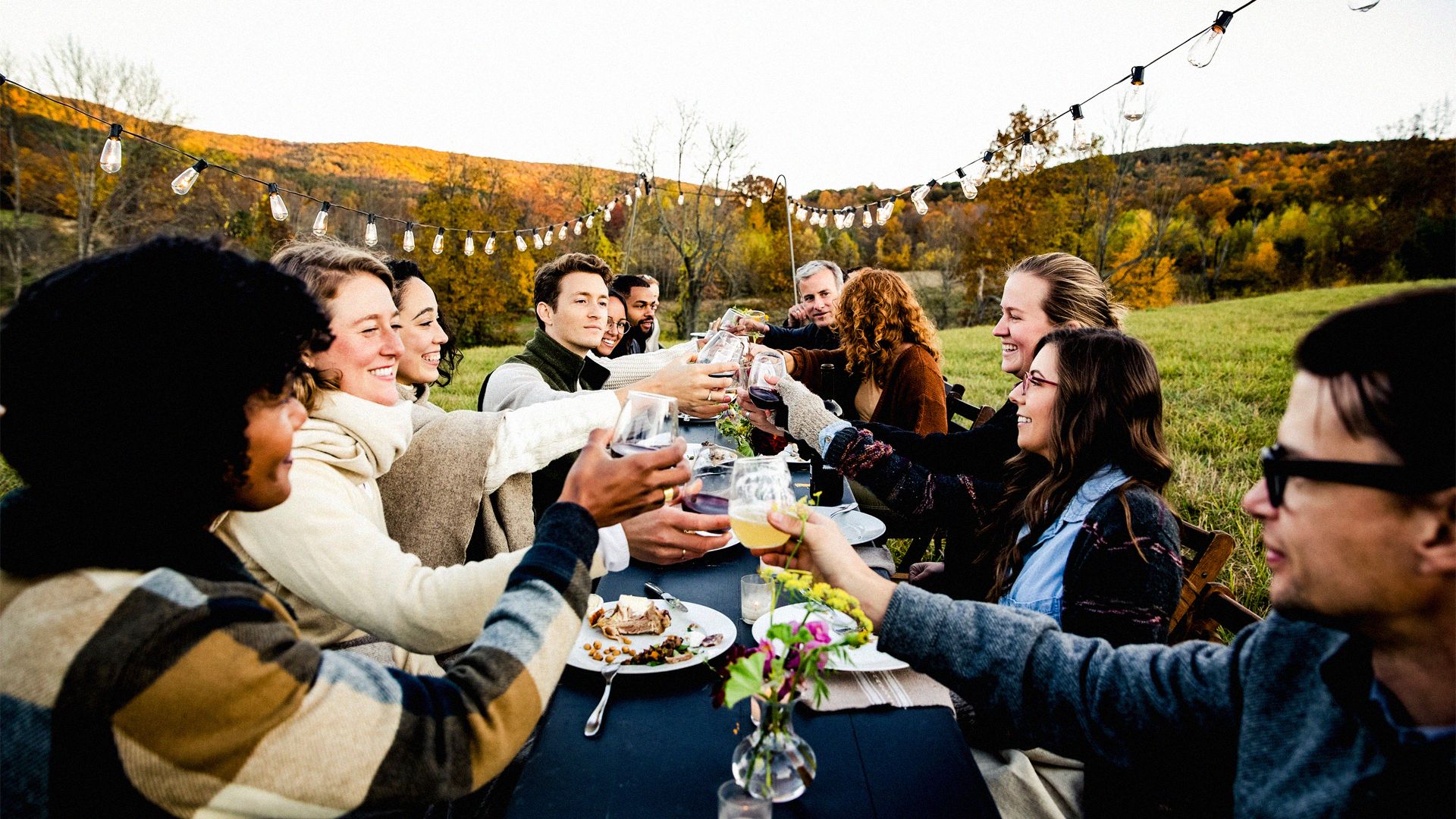 Photo of group of people, seated for an outdoors celebratory meal, toasting the occasion.